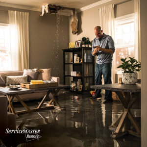 A flooded living room with water pouring from the ceiling, indicating water damage restoration services by ServiceMaster Albino in Waterbury, CT.