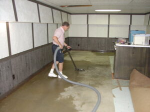 A technician performing water extraction on a wet floor with a rolled-up carpet nearby by Referral Cleaning and Restoration Inc. in Fort Wayne, IN.