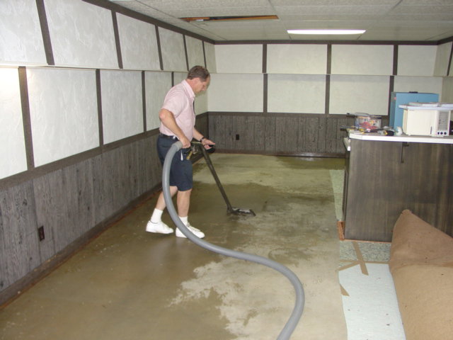 A technician performing water extraction on a wet floor with a rolled-up carpet nearby by Referral Cleaning and Restoration Inc. in Fort Wayne, IN.