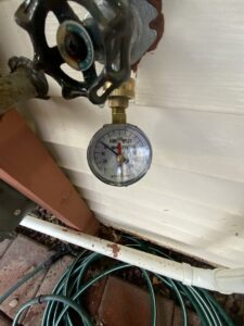 A water pressure gauge connected to an outdoor spigot, indicating plumbing service by Markool Heating Cooling Plumbing in Frederick, MD.
