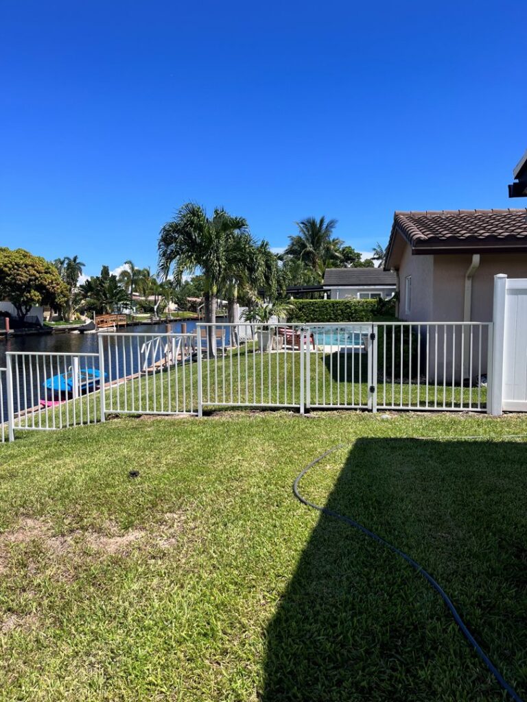 A white metal fence installed along a waterfront property, showcasing a boat, by Ace Fence Company in Fort Lauderdale, FL.