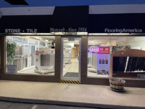 The illuminated storefront of Westcraft Flooring at night, showcasing various carpet and flooring displays in Denver, CO.