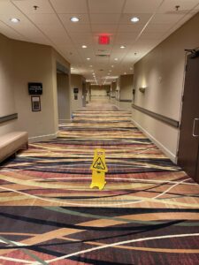 A wet floor sign placed on a freshly cleaned commercial carpet in a hallway by Columbia Carpet Cleaning in Columbia, MO.