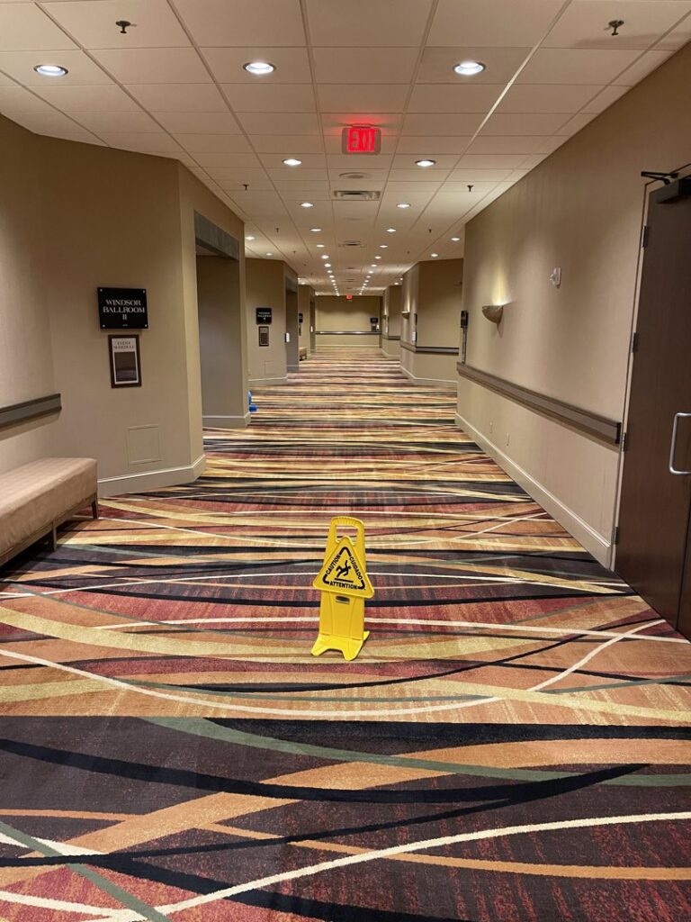 A wet floor sign placed on a freshly cleaned commercial carpet in a hallway by Columbia Carpet Cleaning in Columbia, MO.