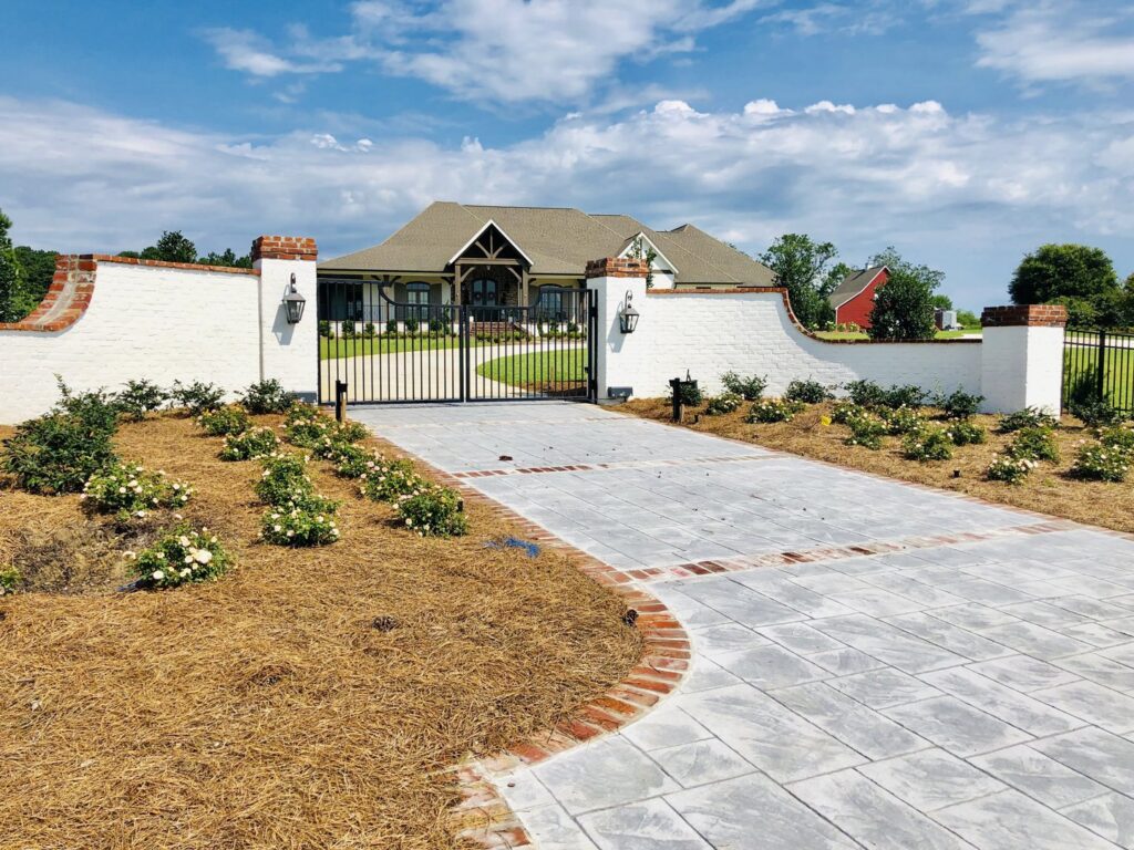 A white brick wall with black metal gates and a paved driveway for a residential property by Jefcoat Fence Co. Inc. of Hattiesburg, MS