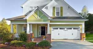 A beautiful light green house featuring a new white carriage-style garage door installed by Frankfort Overhead door Sales & Service in Frankfort, KY