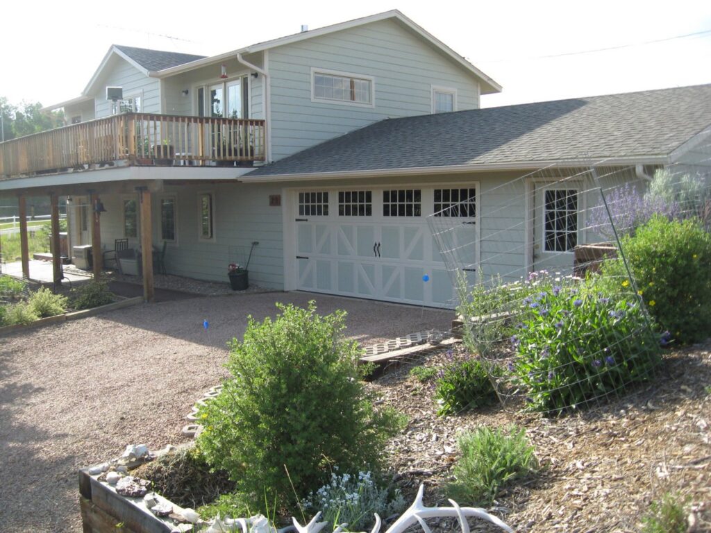 A white carriage-style garage door with windows installed on a light green house by Mountain Fox Garage Doors in Colorado Springs, CO.