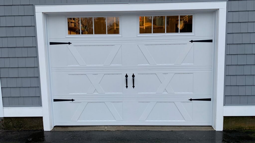 A white carriage-style garage door with decorative hardware and windows installed by PM Garage Door in Hudson, NH.