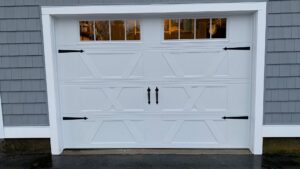 A white carriage-style garage door with decorative hardware and windows installed by PM Garage Door in Hudson, NH.