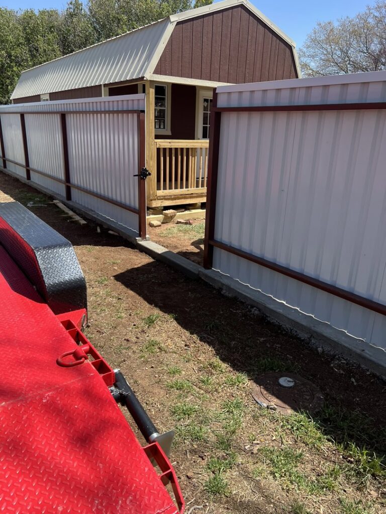 A white corrugated metal fence with an open gate leading to a small shed, a project by DC Fencing LLC in Clovis, NM.