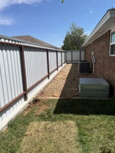 A long white corrugated metal fence running alongside a residential building, installed by DC Fencing LLC in Clovis, NM.