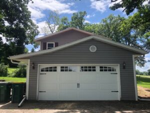 A white garage door with decorative windows and hardware on a gray house, installed by Madison Overhead Garage Door Services in Madison, WI.