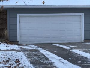 A newly installed white garage door on a gray-sided house, showcasing work by Max Garage Door in Minneapolis, MN.