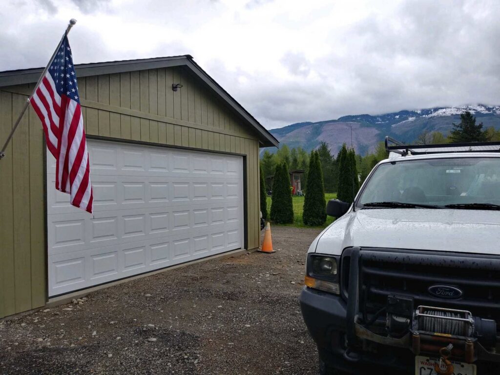 A white garage door installed on a light green building, with a work truck nearby, by Overhead Door Company of Everett, Inc in Everett, WA.