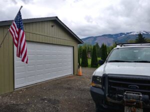 A white garage door installed on a light green building, with a work truck nearby, by Overhead Door Company of Everett, Inc in Everett, WA.