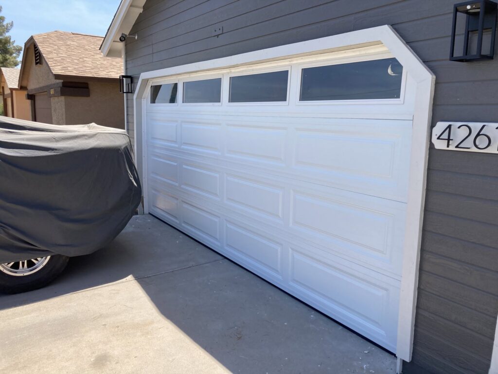 A newly installed white garage door with top windows on a grey house by Anew Garage by Jon's Garages in Surprise, AZ.