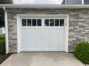 A newly installed white garage door with multiple windows on a stone-faced house by Steve's Overhead Door Company in Lafayette, IN.