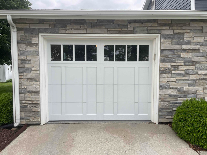 A newly installed white garage door with multiple windows on a stone-faced house by Steve's Overhead Door Company in Lafayette, IN.
