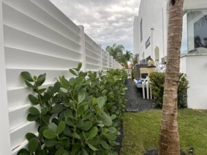 A long white horizontal slat fence with lush green bushes installed by Miami Fence Installation Contractors in Miami, FL.