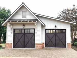 A charming white house with two dark brown carriage-style garage doors installed by Monroe Overhead Doors in Monroe, LA.