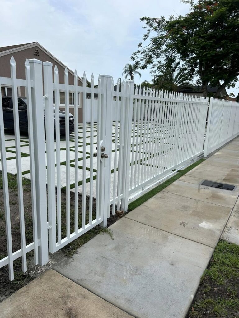 A long white metal picket fence with a pedestrian gate installed along a sidewalk by A Master Work Corp. in Hialeah, FL.