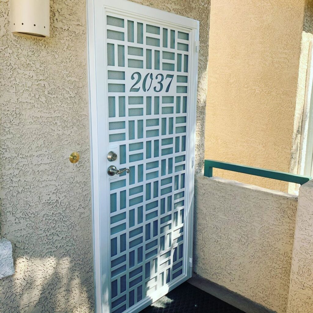 A white metal security door with a modern geometric pattern and house number, installed by Custom Customs Inc. in Henderson, NV.