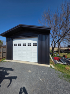 A white panel garage door with windows installed on a dark metal carport structure by APEX Garage Doors and Carports in Lawton, OK.