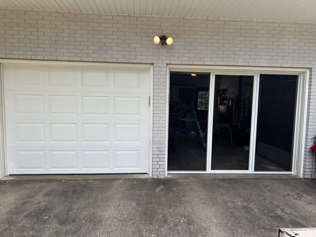 A white panel garage door installed next to a sliding glass door by PM Garage Door in Hudson, NH.