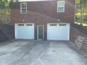Two classic white panel garage doors with windows on a brick residential home by Summers Garage Door in Denver, CO.