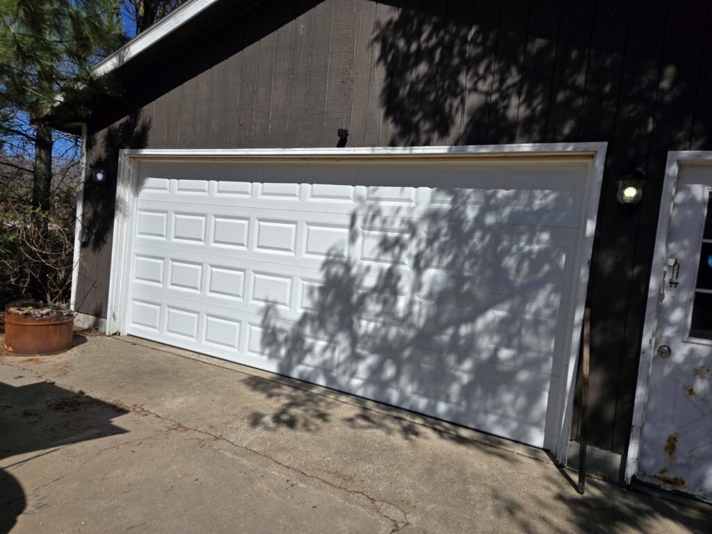 A white paneled garage door installed on a brown wooden building by LabraDoor Overhead Services in Eau Claire, WI.