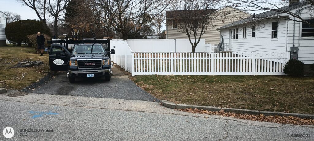 Installation of white picket and privacy fences with a work truck on site by Reilly Fence Inc in Cranston, RI.