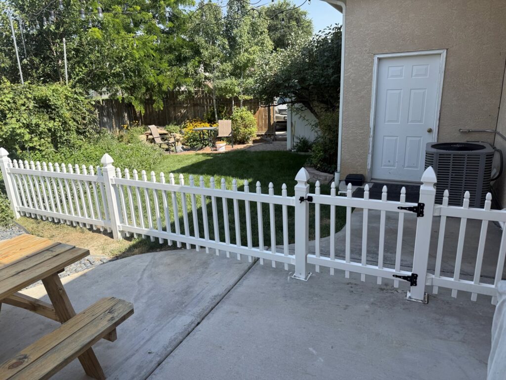 A white picket fence and gate installation in a backyard by Pueblo Fence Co in Pueblo West, CO.