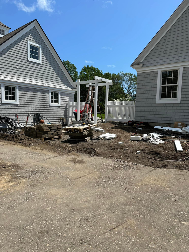 Installation of a white picket fence and matching arbor at a residential property by New England landscaping and fence inc in Lynn, MA.