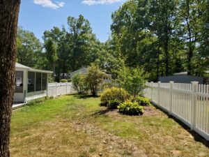 A classic white picket fence enclosing a lush green backyard, installed by MH Fence in Weare, NH.