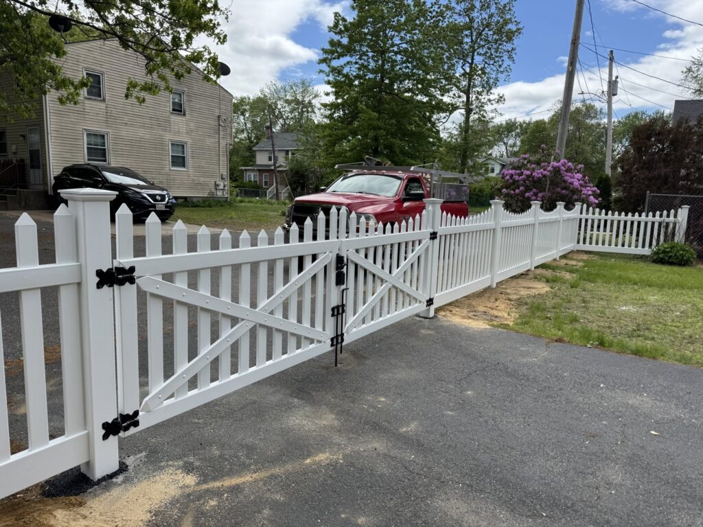 A white picket fence with a large double gate installed across a driveway by Texeira Fencing & Concrete in Springfield, MA.