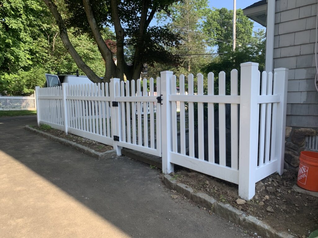 A freshly installed white picket fence with a gate bordering a driveway, completed by AVA Fence & Railing LLC in Stamford, CT.