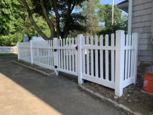 A freshly installed white picket fence with a gate bordering a driveway, completed by AVA Fence & Railing LLC in Stamford, CT.