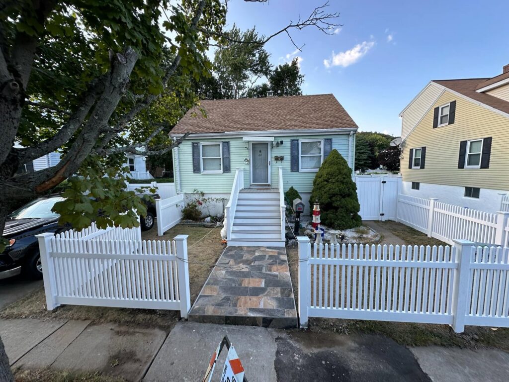 A charming small house with a newly installed white picket fence enclosing the front yard by New England landscaping and fence inc in Lynn, MA.