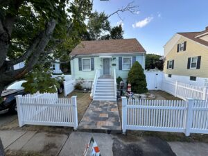 A charming small house with a newly installed white picket fence enclosing the front yard by New England landscaping and fence inc in Lynn, MA.