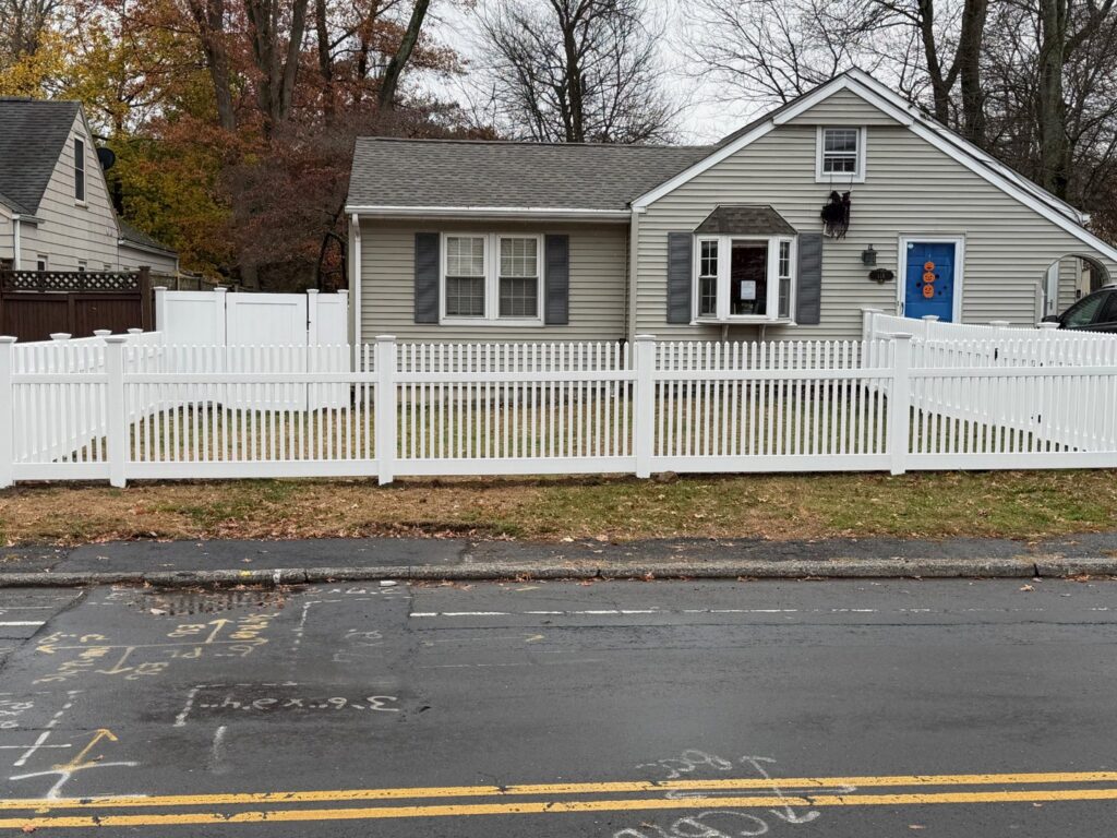 A beautiful white picket fence installed in a front yard along a street by AVA Fence & Railing LLC in Stamford, CT.