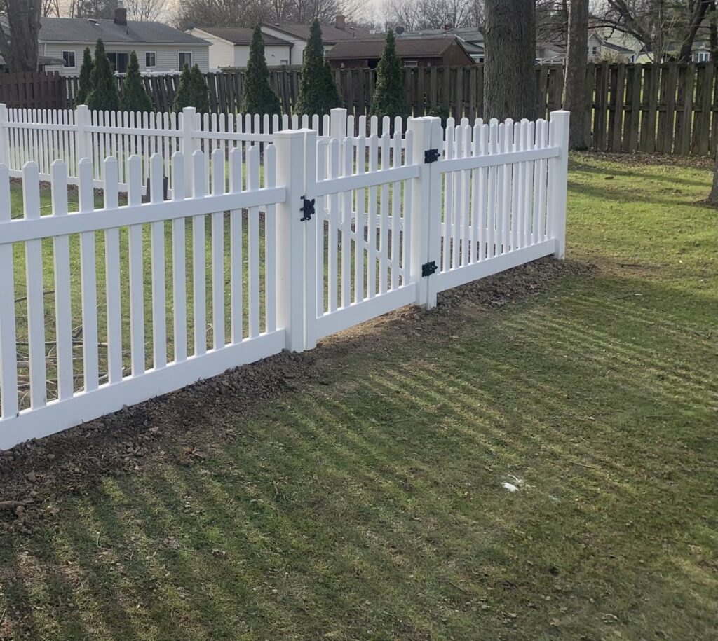 A white picket fence with a gate installed in a residential backyard by Budget Fence of Ohio in Cleveland, OH.