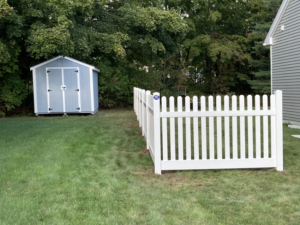 A classic white picket fence installed in a green grassy yard next to a shed by Profence in Leander, TX.