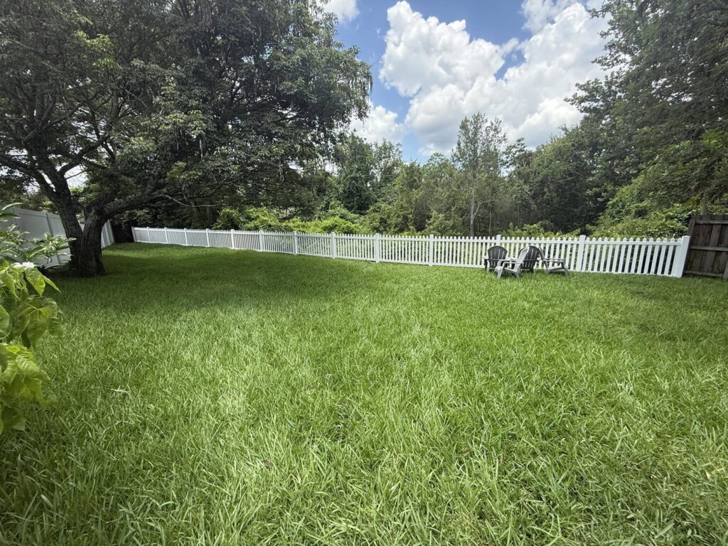 A charming white picket fence installed in a spacious backyard by Native Outdoors, LLC in Orlando, FL.