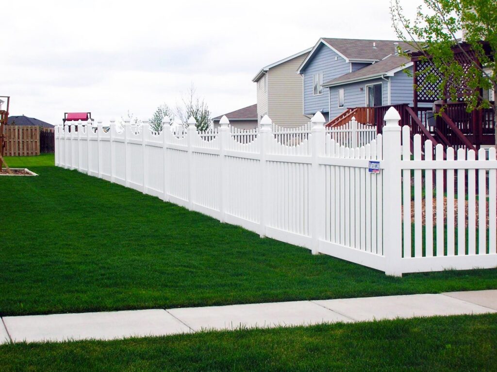 A classic white picket fence installed along a sidewalk in a residential area by American Fence Company - Omaha in Omaha, NE.