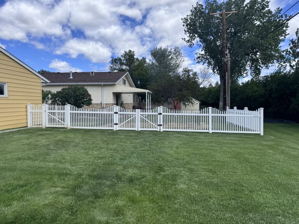 A white picket fence with two gates installed in a backyard by Western Fence in Hebron, ND.