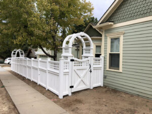 A charming white picket fence with decorative archways and a gate, expertly installed by North CO Fence & Deck in Greeley, CO.