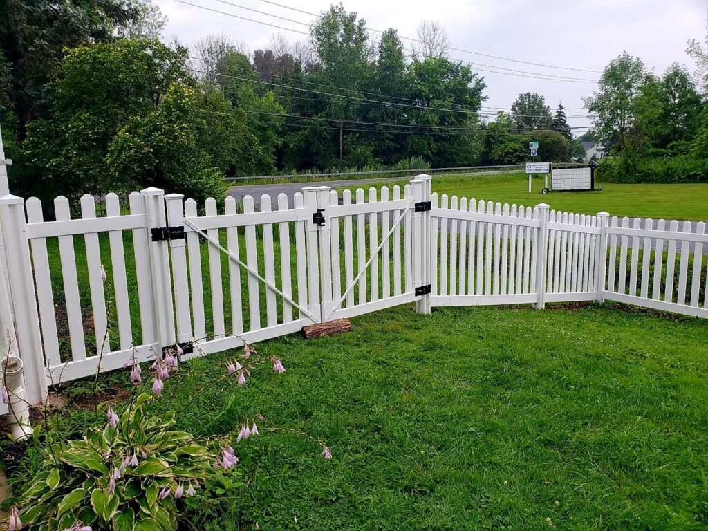 A classic white picket fence with a gate installed in a residential yard by Camp Carlson Fencing in Rochester, NY.