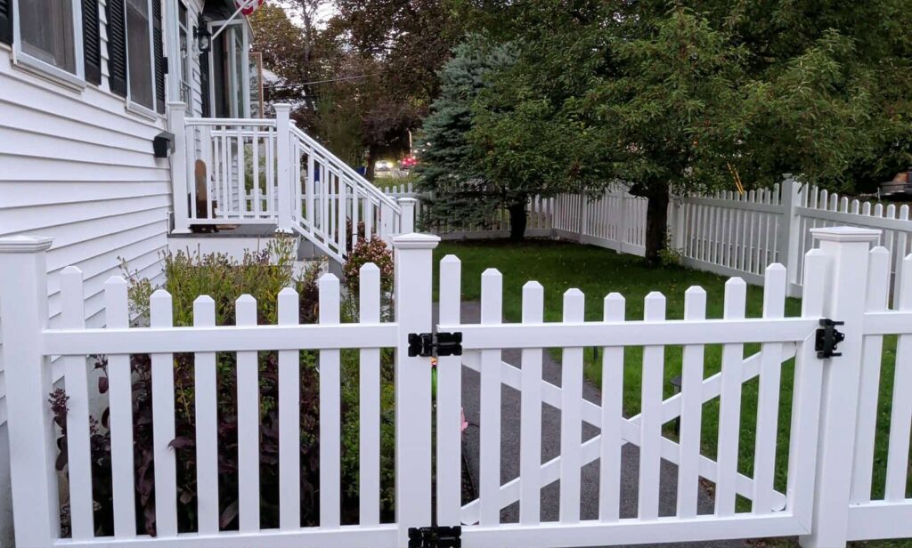 A classic white picket fence with a gate installed in front of a home by Precision Fence NH in Hooksett, NH.