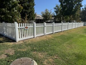 A classic white picket fence with a matching gate installed along a residential property by Mega Fence in Thornton, CA.