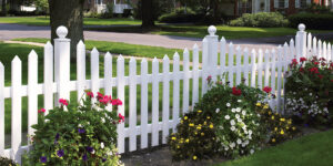 A charming white picket fence with vibrant landscaping installed by Austintown Fence in Youngstown, OH.